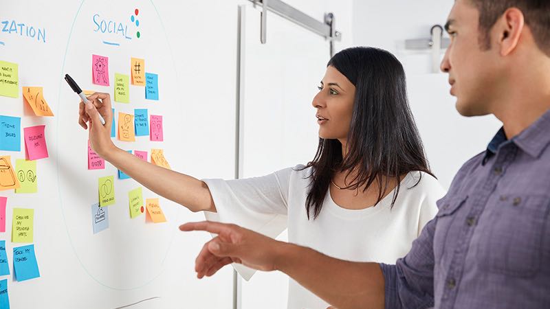 Man and woman brainstorming at Scrum task board.