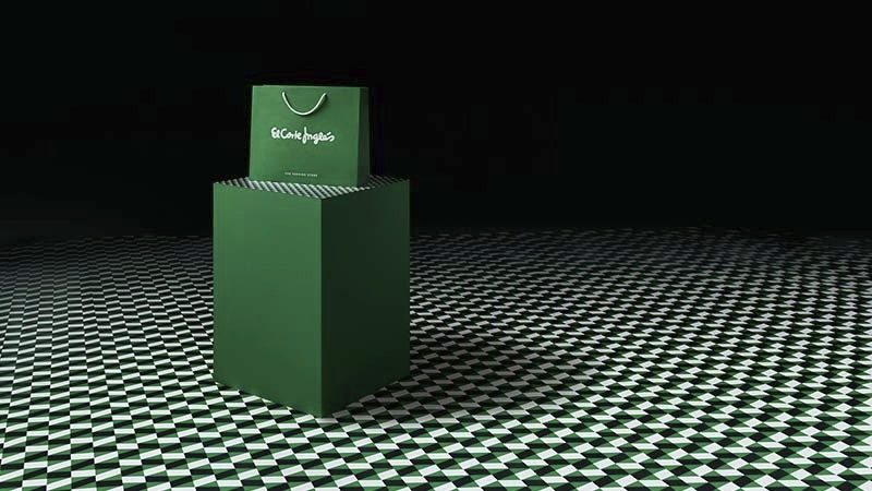 A green shopping bag with white text sits on a geometric black-and-white patterned floor, creating a bold contrast.