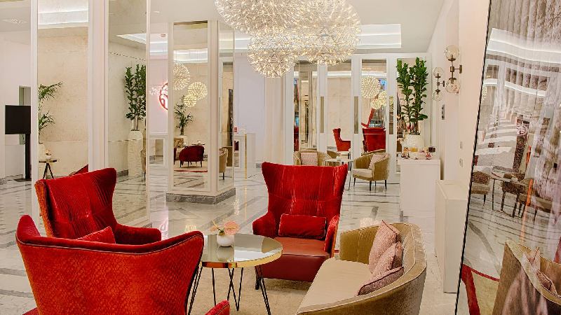 Elegant hotel lobby with red armchairs, mirrored walls, and sparkling chandeliers