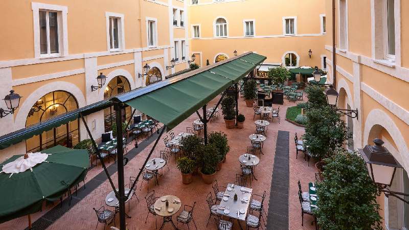 Charming hotel courtyard with outdoor dining tables, green awnings, and potted trees