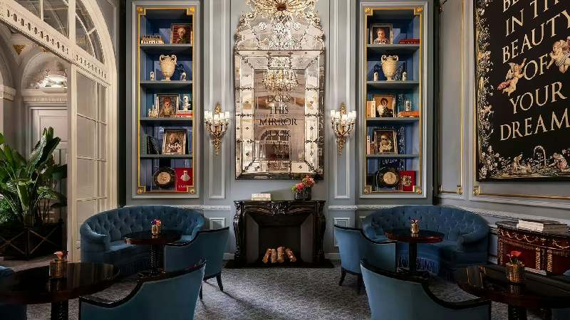 Elegant lounge with blue velvet chairs, ornate mirror, and decorative bookshelves
