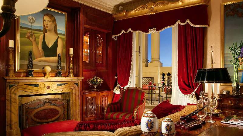 Luxurious classic suite with red velvet drapes, ornate fireplace, and elegant furnishings
