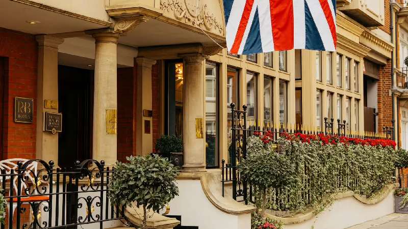 Elegant hotel entrance with stone columns, floral planters, and a Union Jack flag