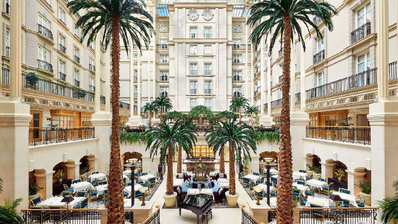 Luxurious hotel atrium with tall palm trees, elegant dining area, and grand interior architecture