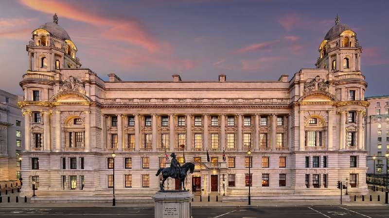 Grand neoclassical building illuminated at dusk with an equestrian statue in front