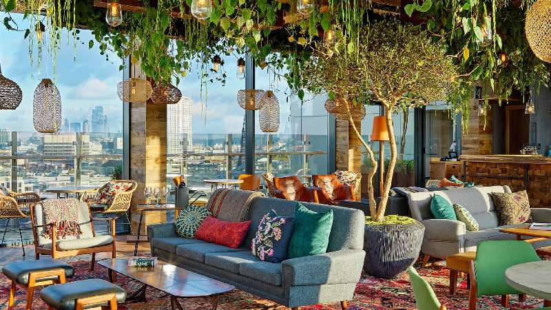 Stylish rooftop lounge with lush greenery, colorful seating, and panoramic city views