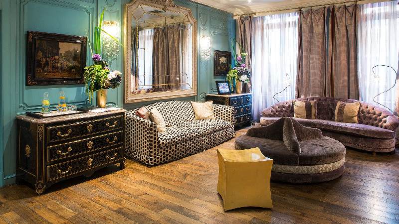 Elegant vintage-style hotel suite with plush seating, ornate mirror, and turquoise walls
