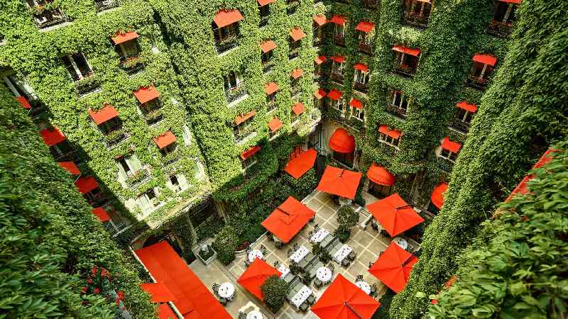 Courtyard of an ivy-covered hotel with red awnings and outdoor seating