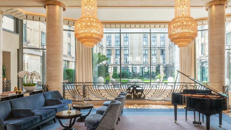 Elegant hotel lounge with chandeliers, grand piano, and courtyard view