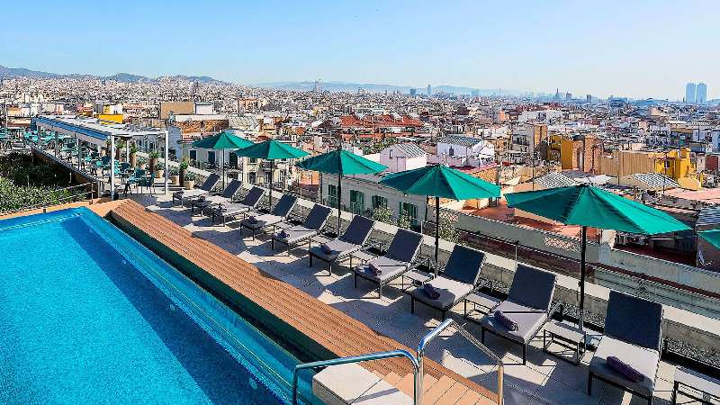 Rooftop pool with sun loungers and umbrellas overlooking a sprawling city skyline