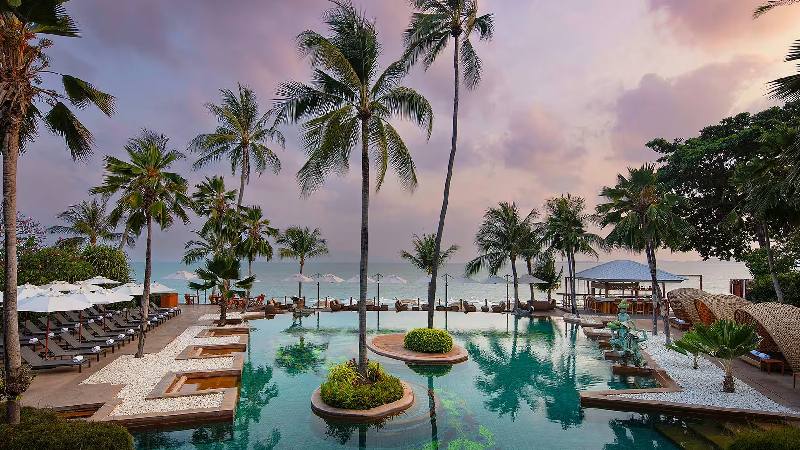 Tropical resort pool surrounded by palm trees at sunset by the beach