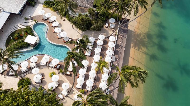 Aerial view of a beachfront resort with pool, palm trees, and lounge umbrellas