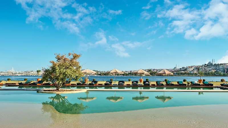 Infinity pool overlooking the water with sun loungers, parasols, and a clear blue sky