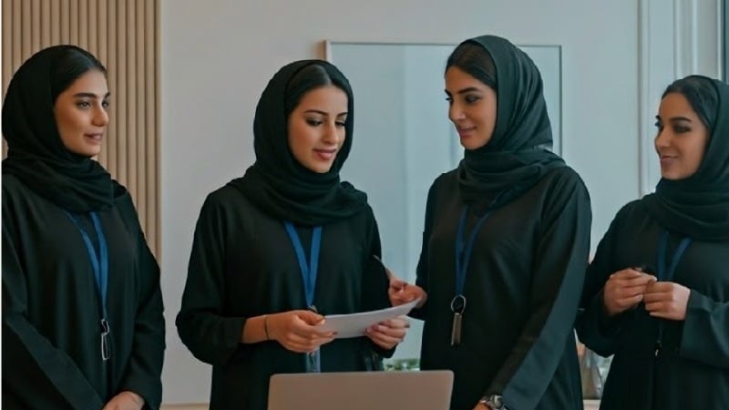 Group of women professionals in traditional attire collaborating around a laptop in an office setting.
