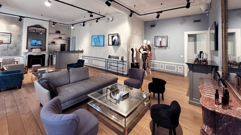 Sophisticated lounge with modern and vintage decor, featuring plush seating, elegant lighting, art on walls, and mannequins in stylish outfits.